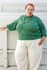 Model wearing Anya Checkerboard Sweater in Fern and Cadence Pants in White, standing in front of white building