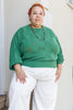 Model wearing Anya Checkerboard Sweater in Fern and Cadence Pants in White, standing in front of white building