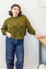 Anya Checkerboard Sweater in Fennel paired with denim jeans on model leaning on table in front of white background