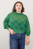 Model wearing Anya Checkerboard Sweater in Fern and denim jeans, standing with hand in pocket in front of white background