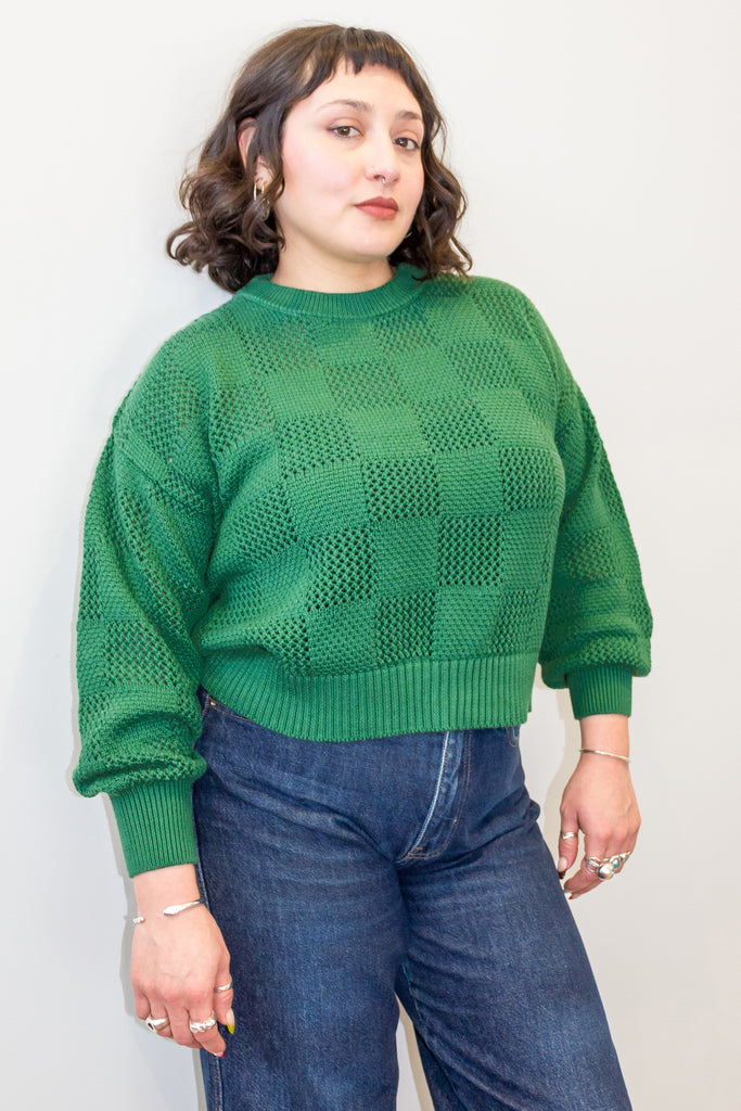 Model wearing Anya Checkerboard Sweater in Fern and denim jeans, in front of white background