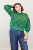 Model wearing Anya Checkerboard Sweater in Fern and denim jeans, in front of white background