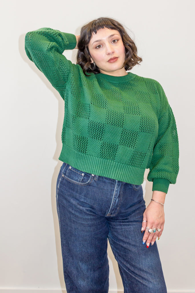 Model wearing Anya Checkerboard Sweater in Fern and denim jeans, in front of white background
