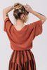 Back view of model wearing Ayana Top in Terracotta and Jessie Skirt in Terracotta Stripe, standing with hands on top of head in front of white background