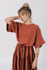 Front view of model wearing Ayana Top in Terracotta and Jessie Skirt in Terracotta Stripe, standing with one hand behind neck in front of white background