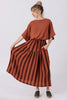 Front view of model wearing Ayana Top in Terracotta and Jessie Skirt in Terracotta Stripe, standing with one hand holding out skirt in front of white background