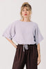 Front view of model wearing Ayana Top in Mist and Cadence Pant in Chocolate, standing with one hand in pant pocket in front of white wall