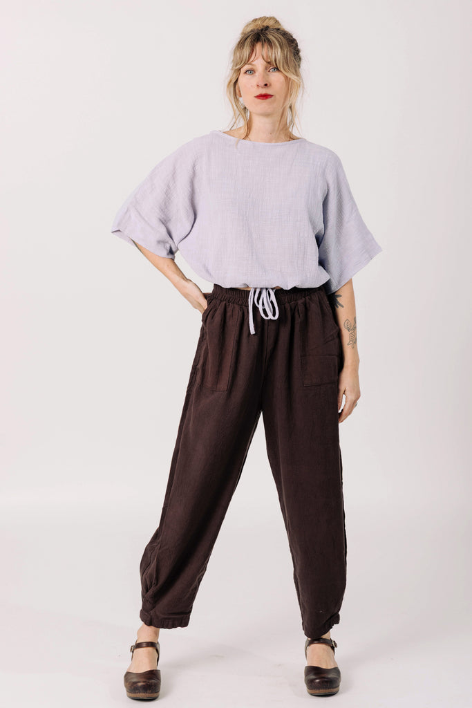 Front view of model wearing Ayana Top in Mist and Cadence Pant in Chocolate, standing with one hand in pants pocket in front of white background
