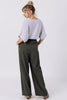 Back view of model wearing Ayana Top in Mist and Atlas Pant in Mud, standing with hands in pants pockets in front of white background