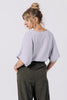 Back view of model wearing Ayana Top in Mist and Atlas Pant in Mud, standing with hands in pant pockets in front of white background