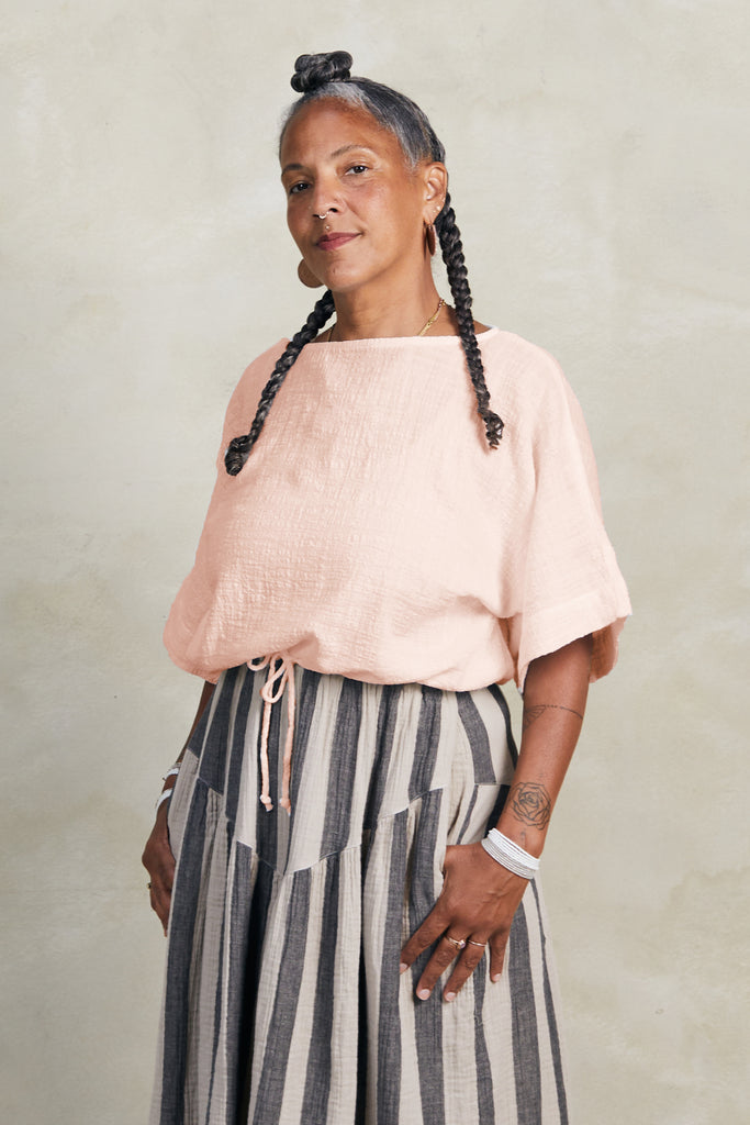 Model wearing Ayana Top in Peach and Jessie Stripe Skirt in Oat, standing in front of white background