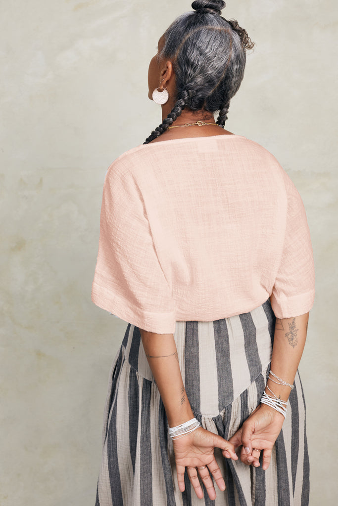 Back view of model wearing Ayana Top in Peach and Jessie Stripe Skirt in Oat, standing with arms behind back, in front of white background