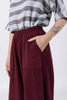 Close up of model wearing Izzy Top in Oyster Stripe and Cadence Pant in Burgundy, with one hand in pant pocket, in front of white background