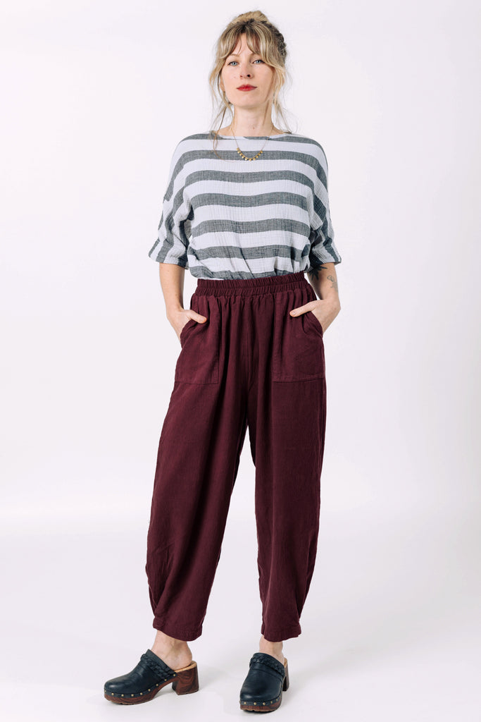 Front view of model wearing Izzy Top in Oyster Stripe and Cadence Pant in Burgundy, standing with hands in pants pockets in front of white background