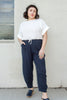 Model wearing Ayana Top in White and Cadence Pant in Black Stripe, standing with one hand in pant pocket in front of white wall