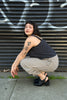 Model wearing Bianca Top in Black and Cadence Pant in Oat/Black Stripe, squatting in front of black garage door with white spray paint at the top