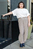 Model wearing Ayana Top in White and Cadence Pant in Oat Stripe, standing with one hand hand railing of black tiled entryway