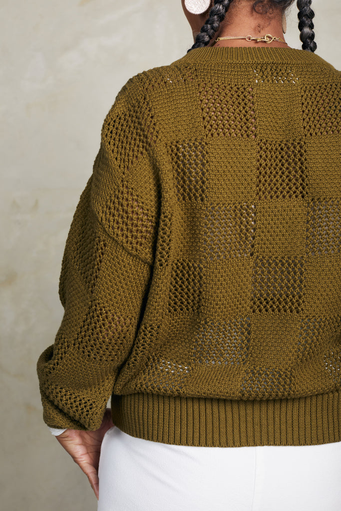 Back view of model wearing Anya Checkerboard Sweater in Fennel in front of white background
