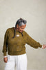 Model wearing Anya Checkerboard Sweater In Fennel and Atlas Pant in White in front of white background