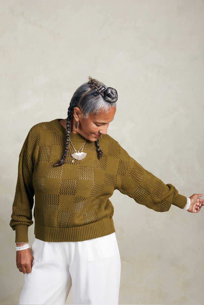 Model wearing Anya Checkerboard Sweater In Fennel and Atlas Pant in White in front of white background