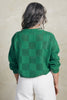 Back view of model wearing Anya Checkerboard Sweater In Fern and white jeans in front of white background