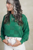 Model wearing Anya Checkerboard Sweater In Fern and white jeans in front of white background