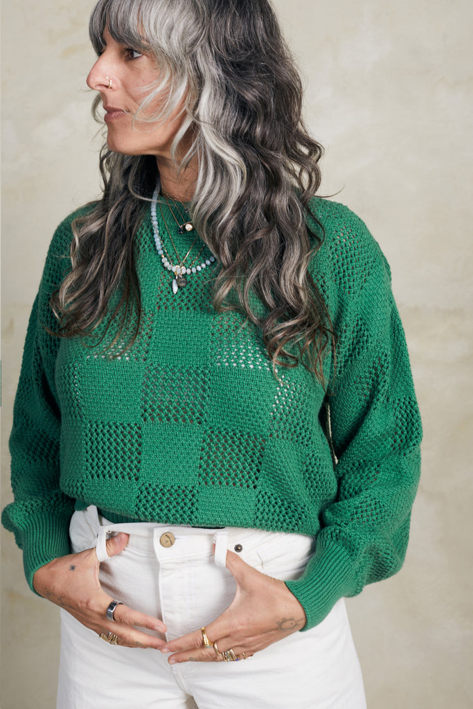 Model wearing Anya Checkerboard Sweater In Fern and white jeans in front of white background
