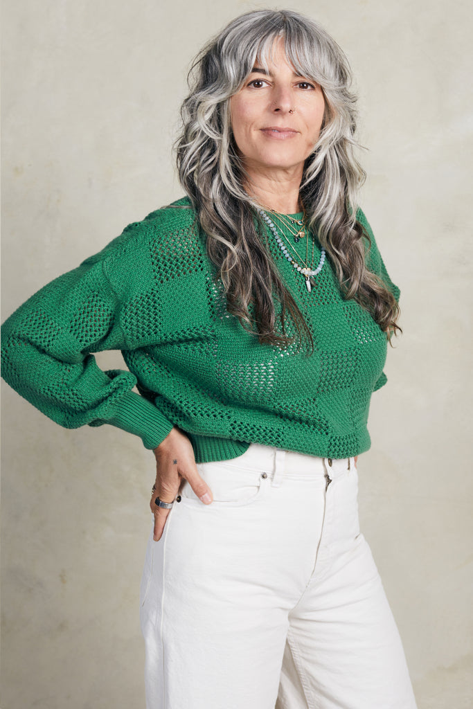 Model wearing Anya Checkerboard Sweater In Fern and white jeans in front of white background