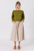 Front view of model wearing Clove Sweater in Fennel and Fawn Skirt in Oat with hands in skirt pockets in front of white background