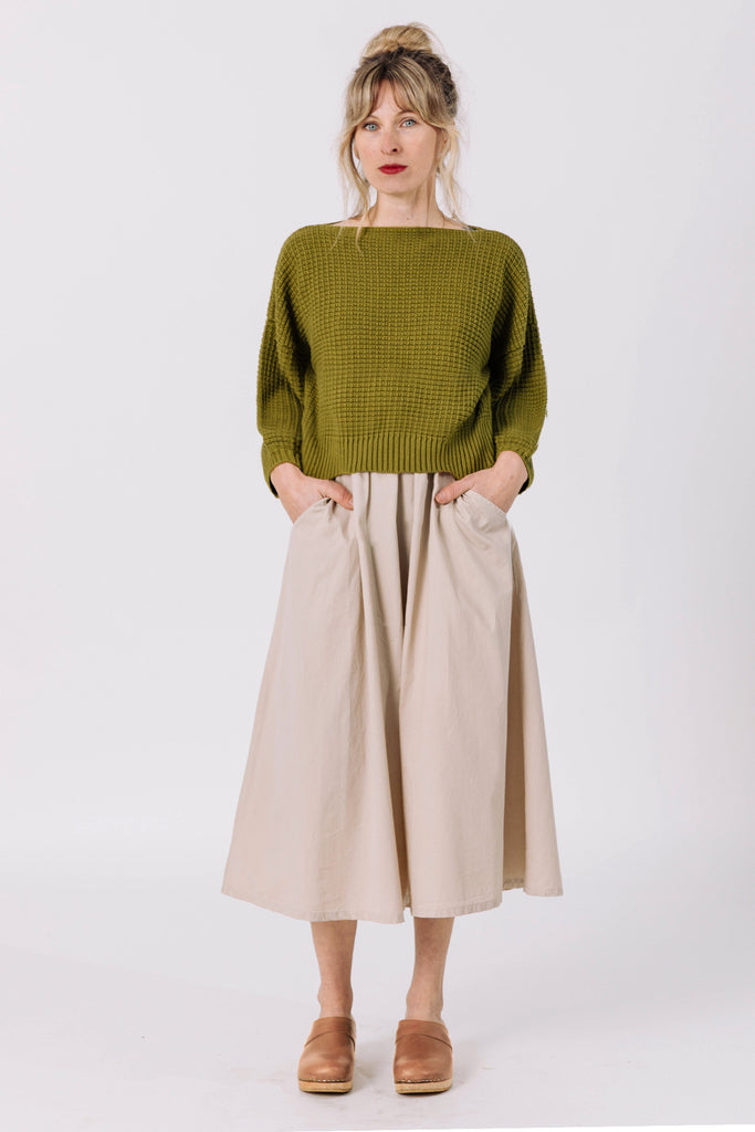 Front view of model wearing Clove Sweater in Fennel and Fawn Skirt in Oat with hands in skirt pockets in front of white background