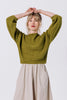 Front view of model with arms over head wearing Clove Sweater in Fennel and Fawn Skirt in Oat in front of white background