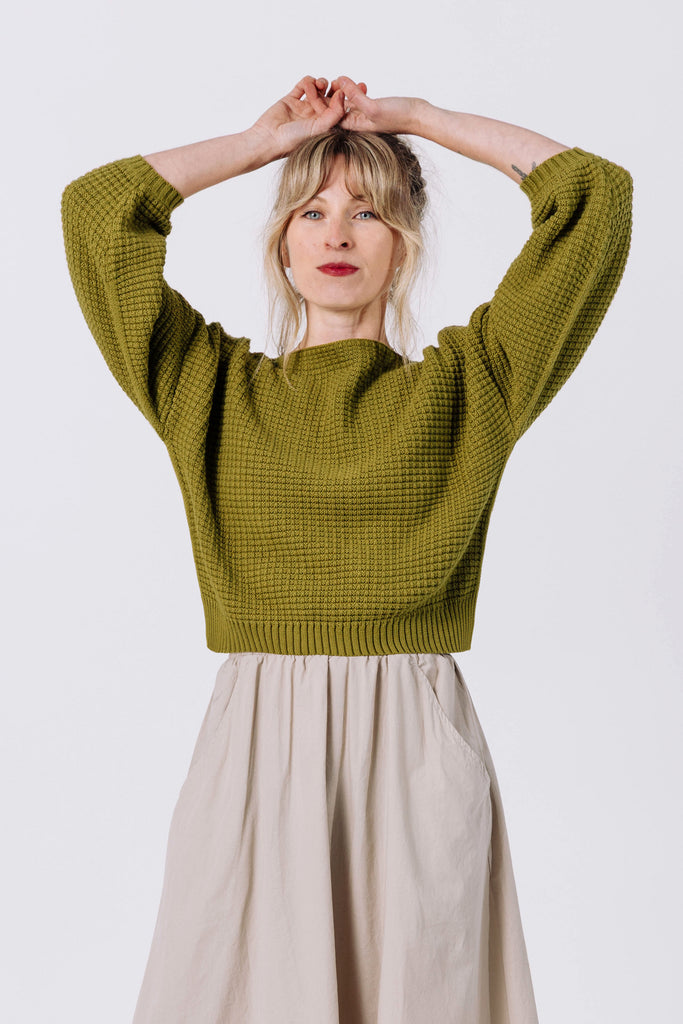 Front view of model with arms over head wearing Clove Sweater in Fennel and Fawn Skirt in Oat in front of white background