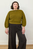 Model wearing Clove Sweater in Fennel and wide leg pants in black standing in front of white background