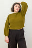 Model wearing Clove Sweater in Fennel and wide leg pants in black with hand raised to head, standing in front of white background