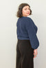 Back/side view of model wearing Clove Sweater in Fennel and wide leg pants in black standing in front of white background