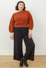 Front view of Atlas Pant in Black on model, paired with Clove Sweater in Paprika, in front of white wall