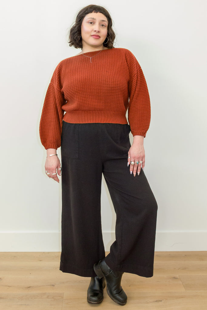 Front view of Atlas Pant in Black on model, paired with Clove Sweater in Paprika, in front of white wall