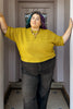 Person wearing a dijon Cody sweater and dark pants standing in a hallway.