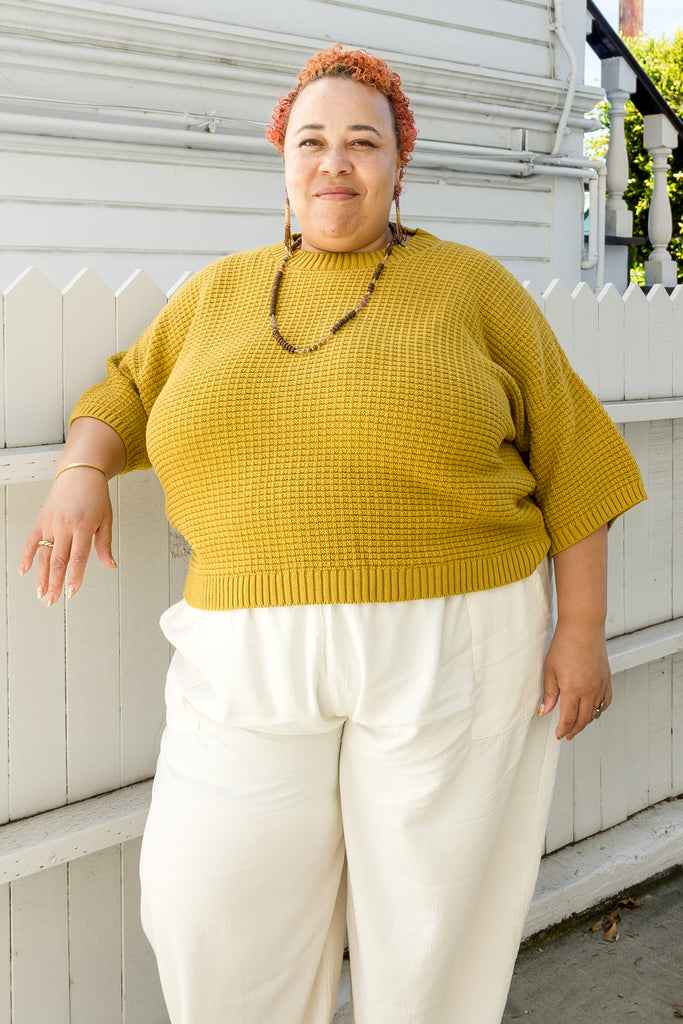 Model wearing Cody Waffle Tee in Dijon and Cadence Pants in White, leaning against a white buidling