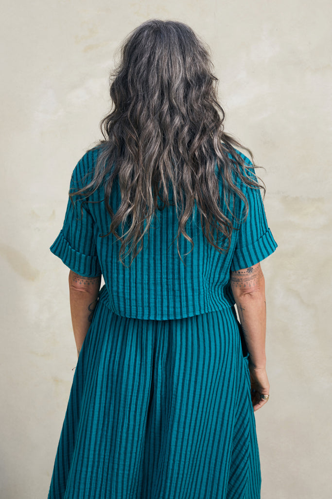 Back view of Noa Stripe Top in Ocean, paired with Fawn Stripe Skirt in Ocean, on model standing in front of white background.