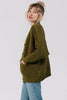Side view of model wearing Frankie Cardigan in Fennel and light wash jeans with hands in cardigan pockets, in front of white background