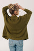 Back view of model wearing Frankie Cardigan in Fennel and light wash jeans, raising arms over head in front of white background