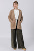 Front view of model wearing Frankie Cardigan in Tan, Ayana Top in White, and Atlas Pant in Mud, standing with hands in cardigan pockets in front of white wall