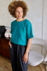 Woman wearing a teal ribbed top and dark pants in an indoor setting.