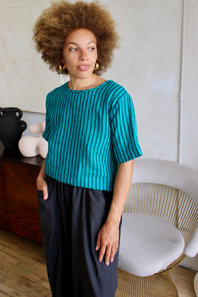 Woman wearing a teal ribbed top and dark pants in an indoor setting.