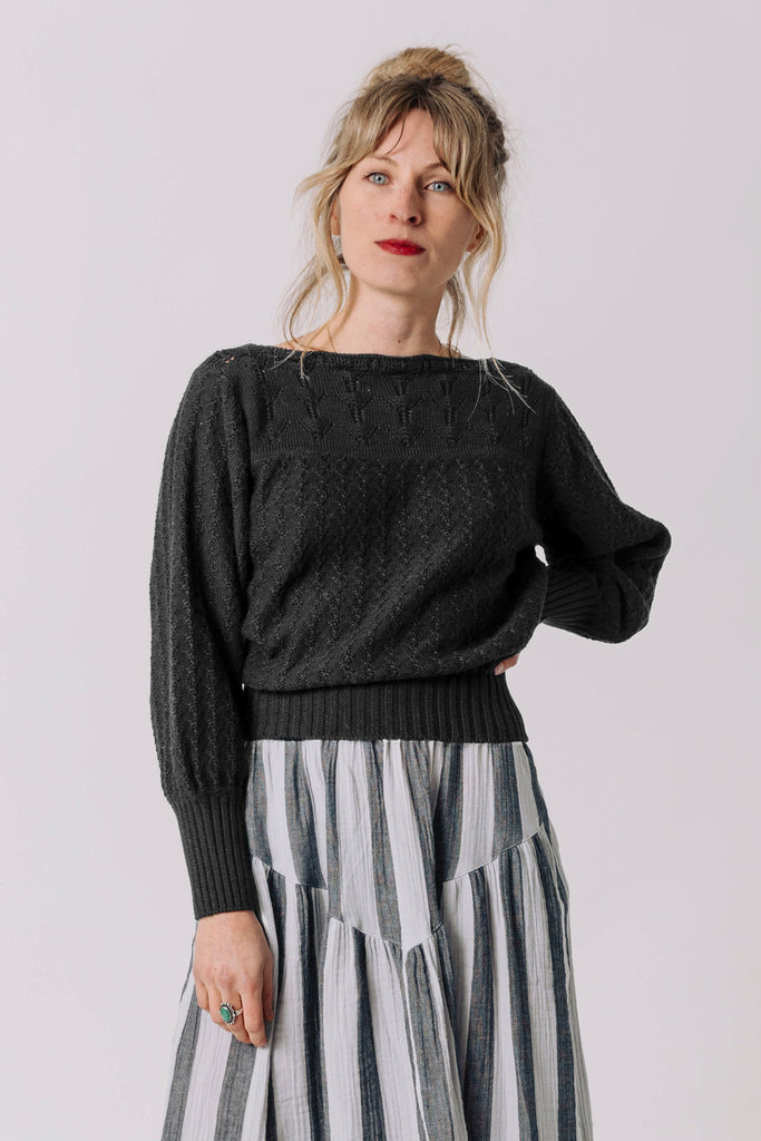 Front view of model wearing Ivy Sweater in Black and Jessie Stripe Skirt in Oyster, with one hand on hip, standing in front of white background