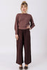 Front view of model wearing Ivy Sweater in Raisin and Atlas Pant in Chocolate, standing with one hand on hip in front of white wall