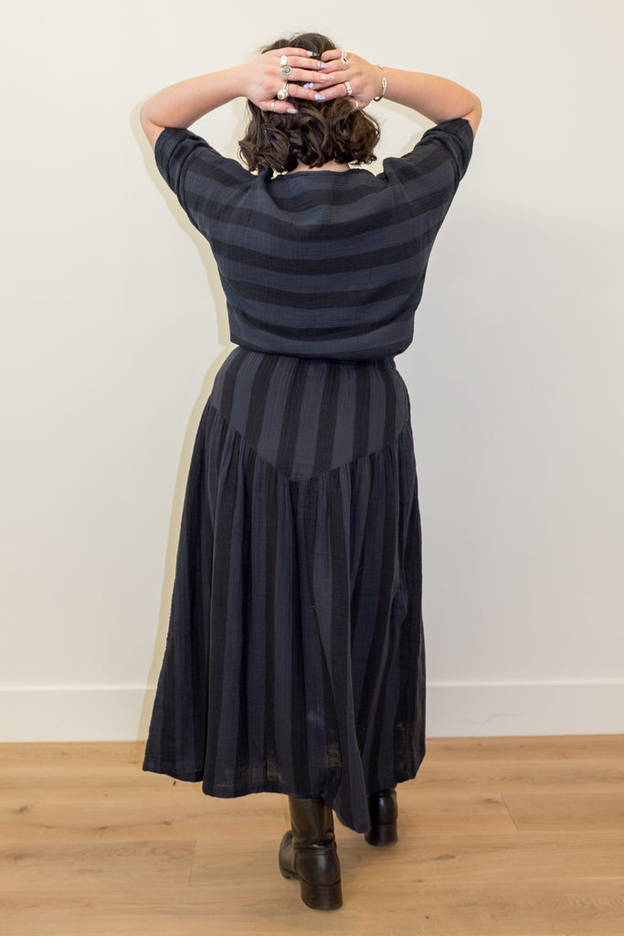 Back view of odel wearing Izzy Top and Jessie Skirt set in Faded Black Stripe standing in front of white wall