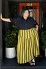 Person wearing a black poet shirt and dijon striped jessie skirt standing in front of a door with a number 506.