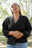 Model wearing Boucle Jonah Cardigan in black and light wash jeans standing in park with tall trees